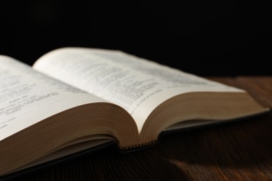 Photo of Open Bible on wooden table against black background, closeup