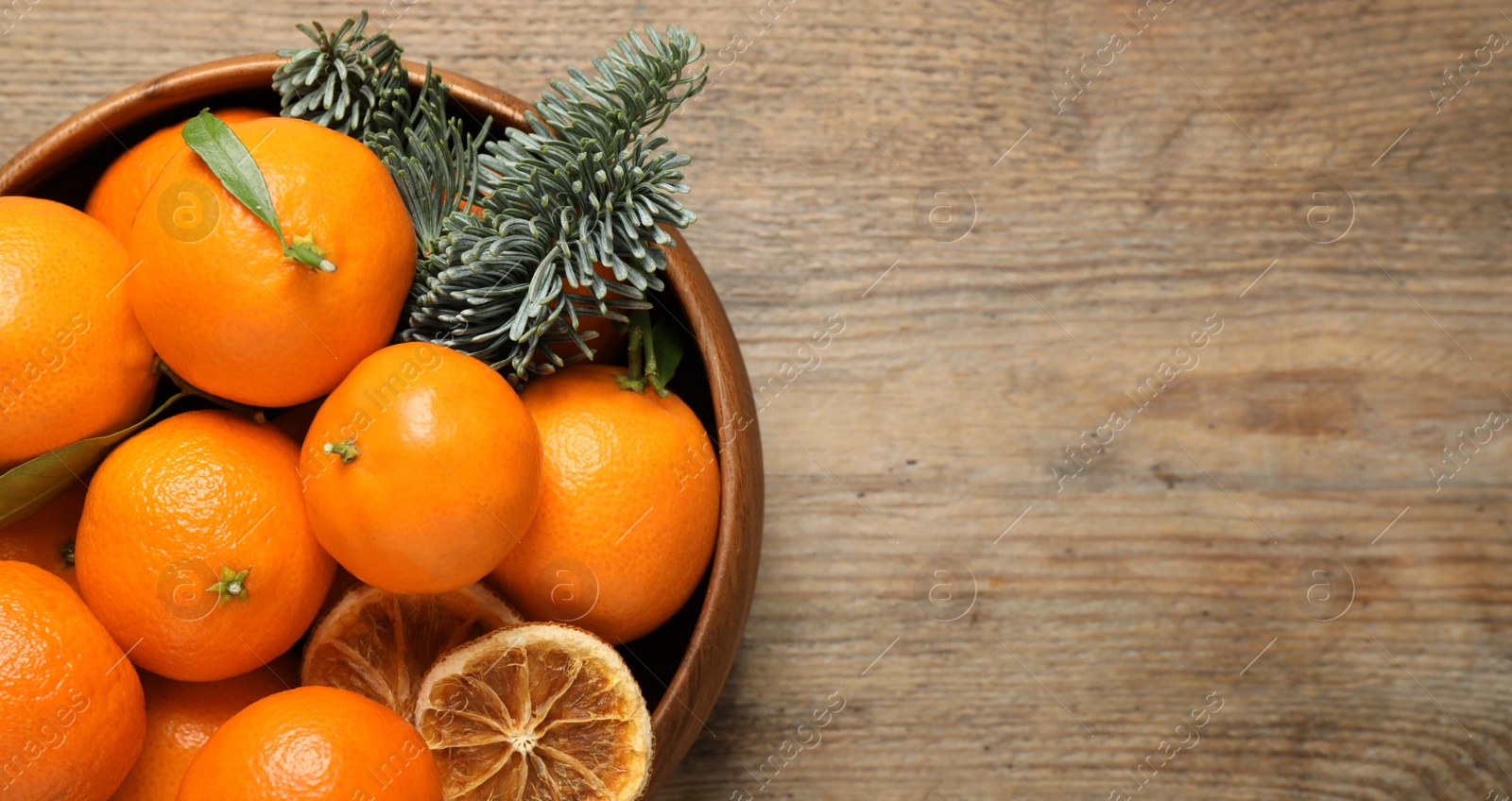 Photo of Fresh tangerines and fir tree branches in bowl on wooden table, top view with space for text. Christmas atmosphere