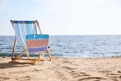 Photo of Lounger and bag on sand near sea, space for text. Beach objects