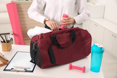 Businesswoman packing sports stuff for training into bag in office, closeup 