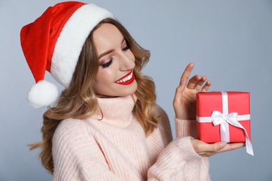 Photo of Happy young woman wearing Santa hat with Christmas gift on grey background