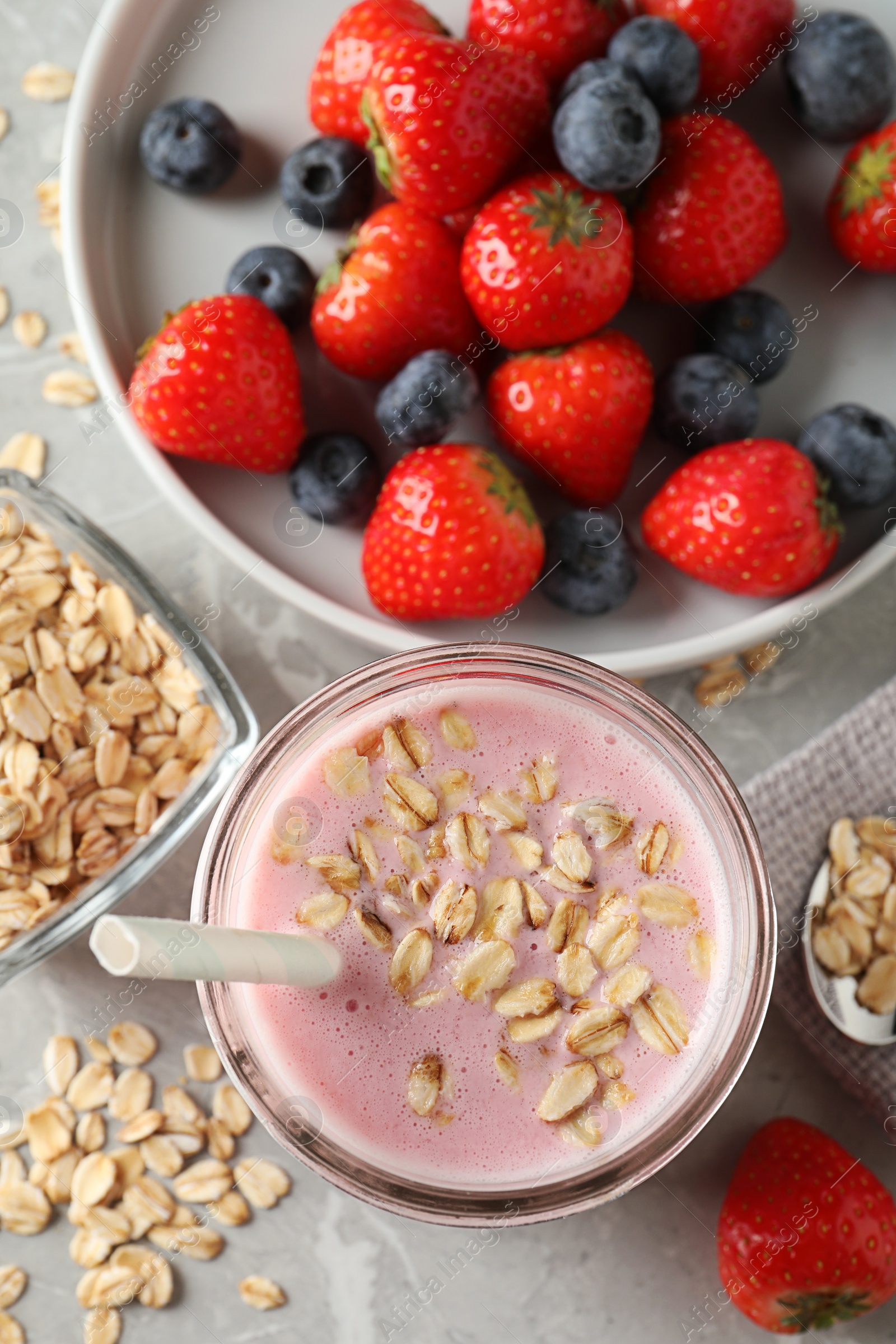 Photo of Jar of tasty berry oatmeal smoothie and ingredients on grey table, flat lay