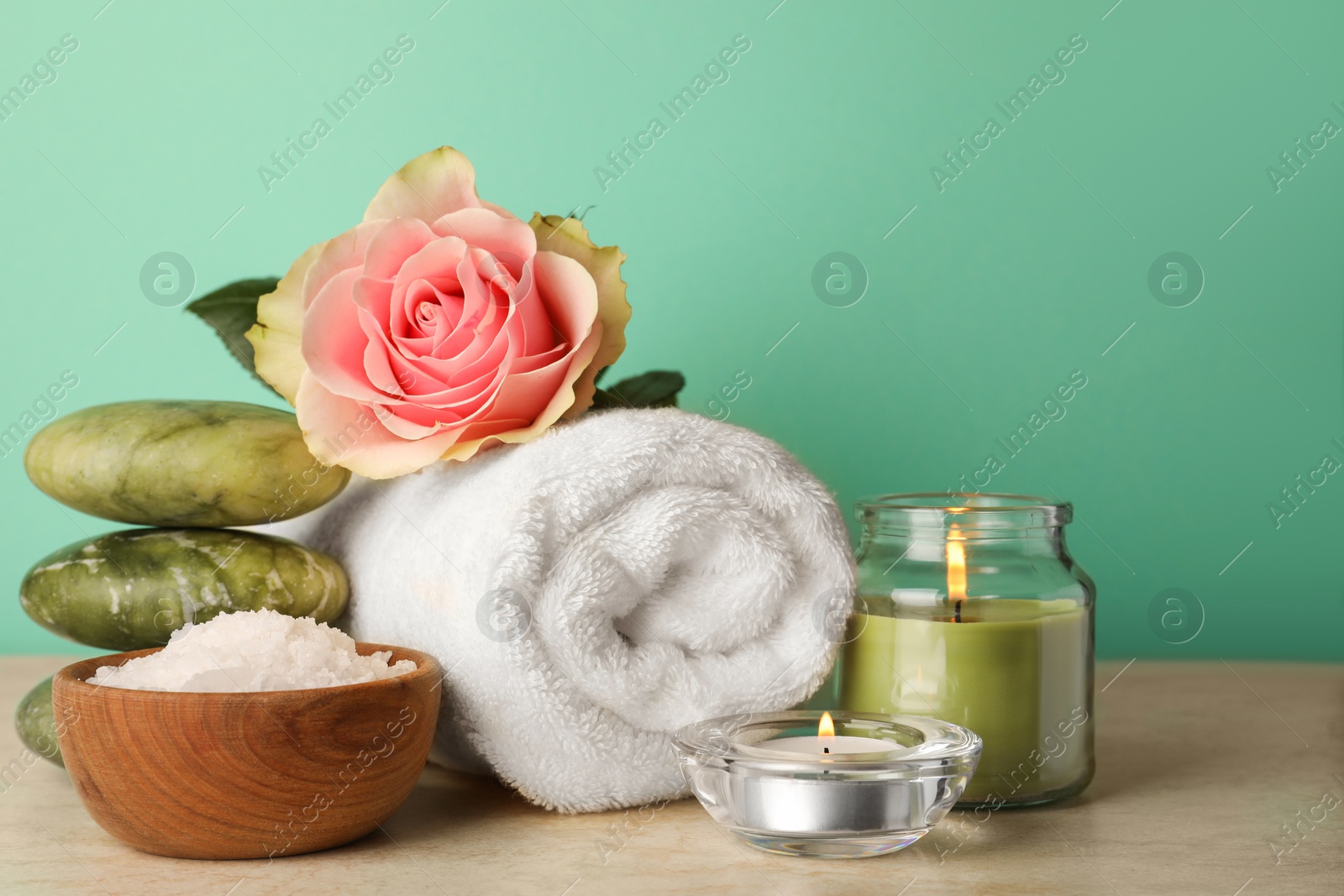 Photo of Composition with different spa products, candles and rose on beige table against turquoise background. Space for text