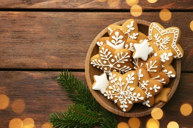 Tasty Christmas cookies with icing in bowl and fir tree branches on wooden table, flat lay. Space for text