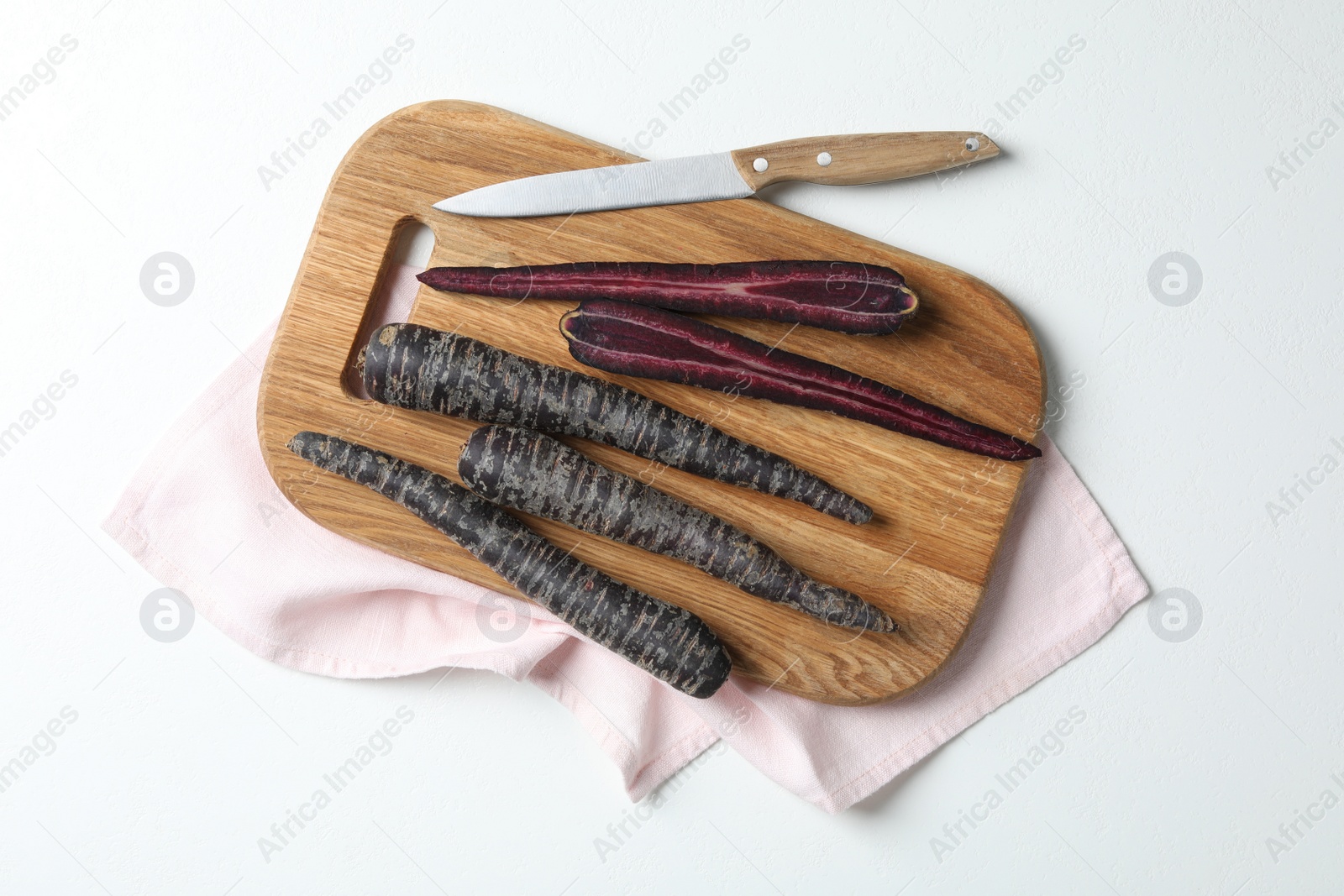 Photo of Raw black carrots, knife and cutting board on white table, flat lay