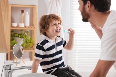 Father and his son brushing teeth together in bathroom