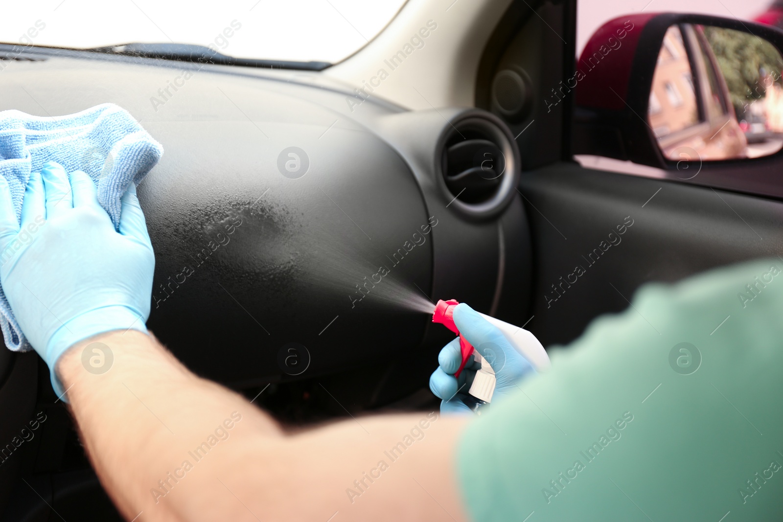 Photo of Man cleaning car salon with disinfectant spray and cloth, closeup