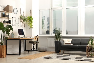 Photo of Cozy workplace with computer and houseplants near sofa at home