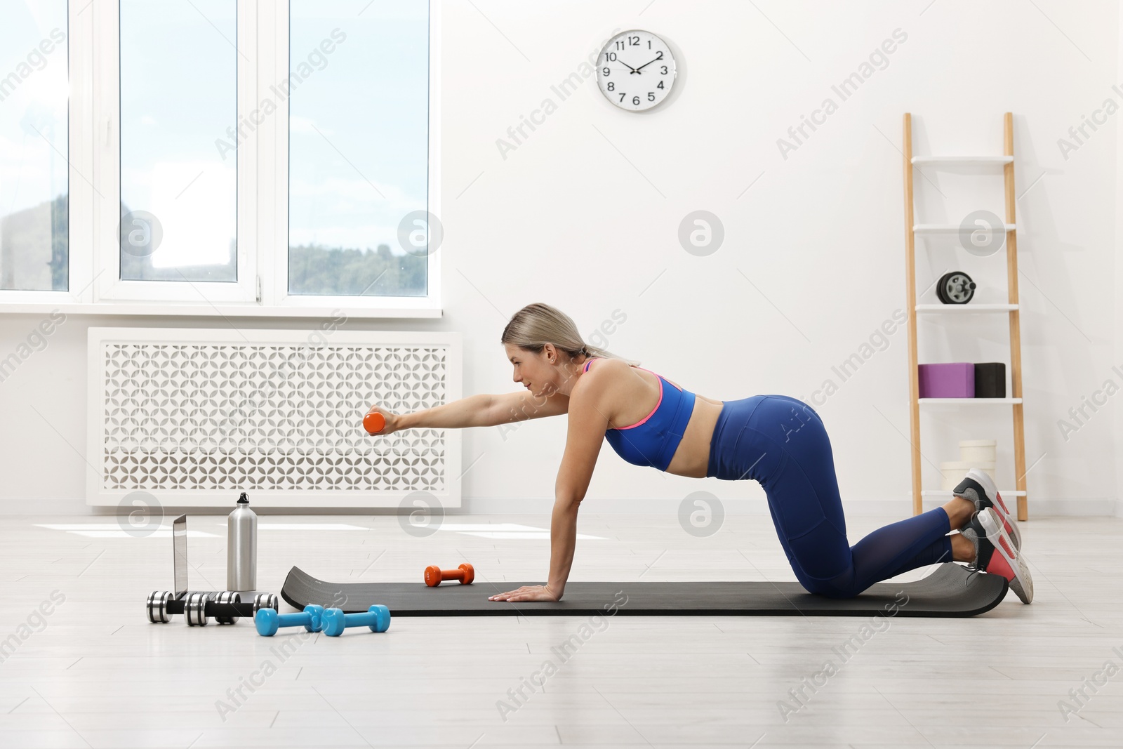 Photo of Online fitness trainer. Woman doing exercise with dumbbells near laptop at home