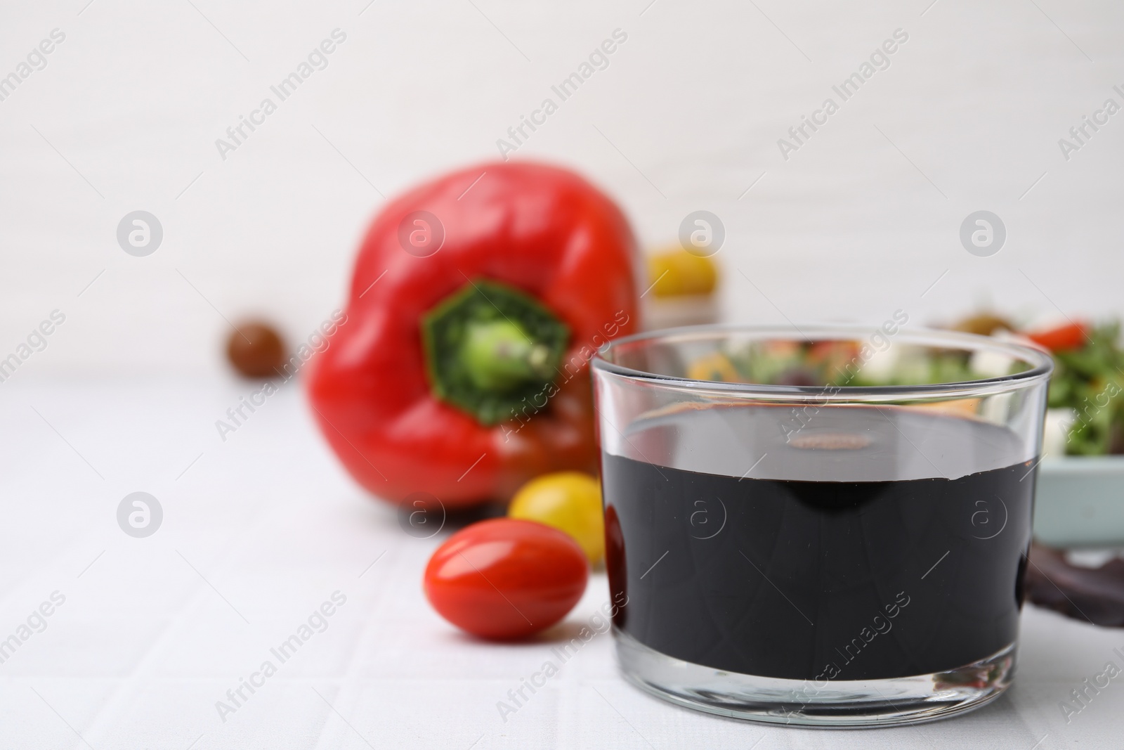 Photo of Vinegar in glass on white tiled table, closeup. Space for text