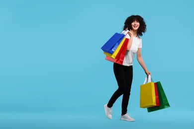 Photo of Happy young woman with shopping bags on light blue background. Space for text