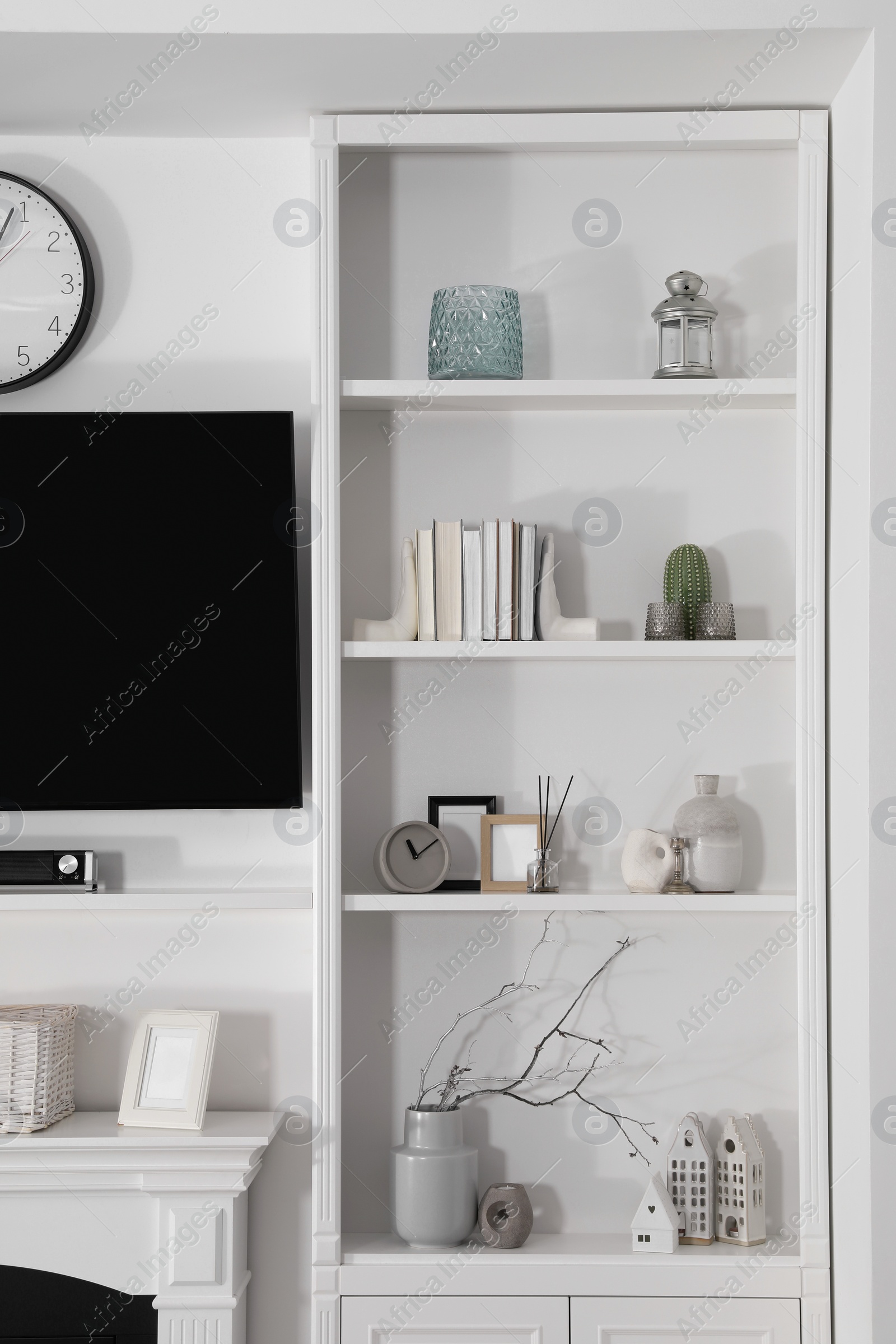 Photo of Stylish shelves with different decor elements and TV set in room. Interior design