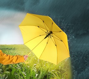 Woman with open yellow umbrella under heavy rain in green field, closeup