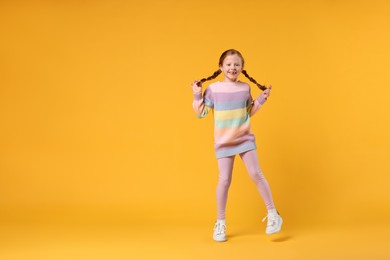 Photo of Cute little girl dancing on orange background, space for text