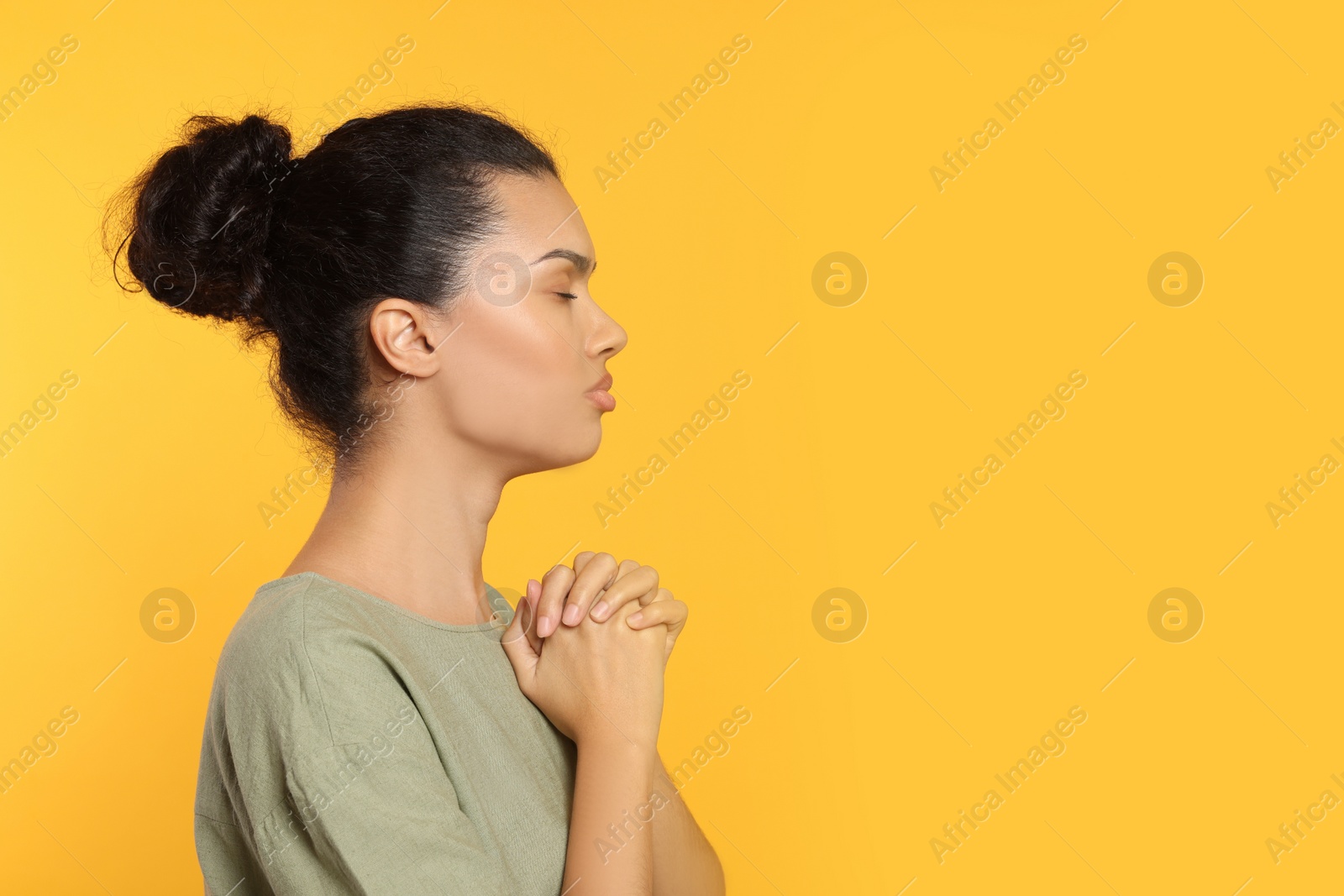 Photo of African American woman with clasped hands praying to God on orange background. Space for text