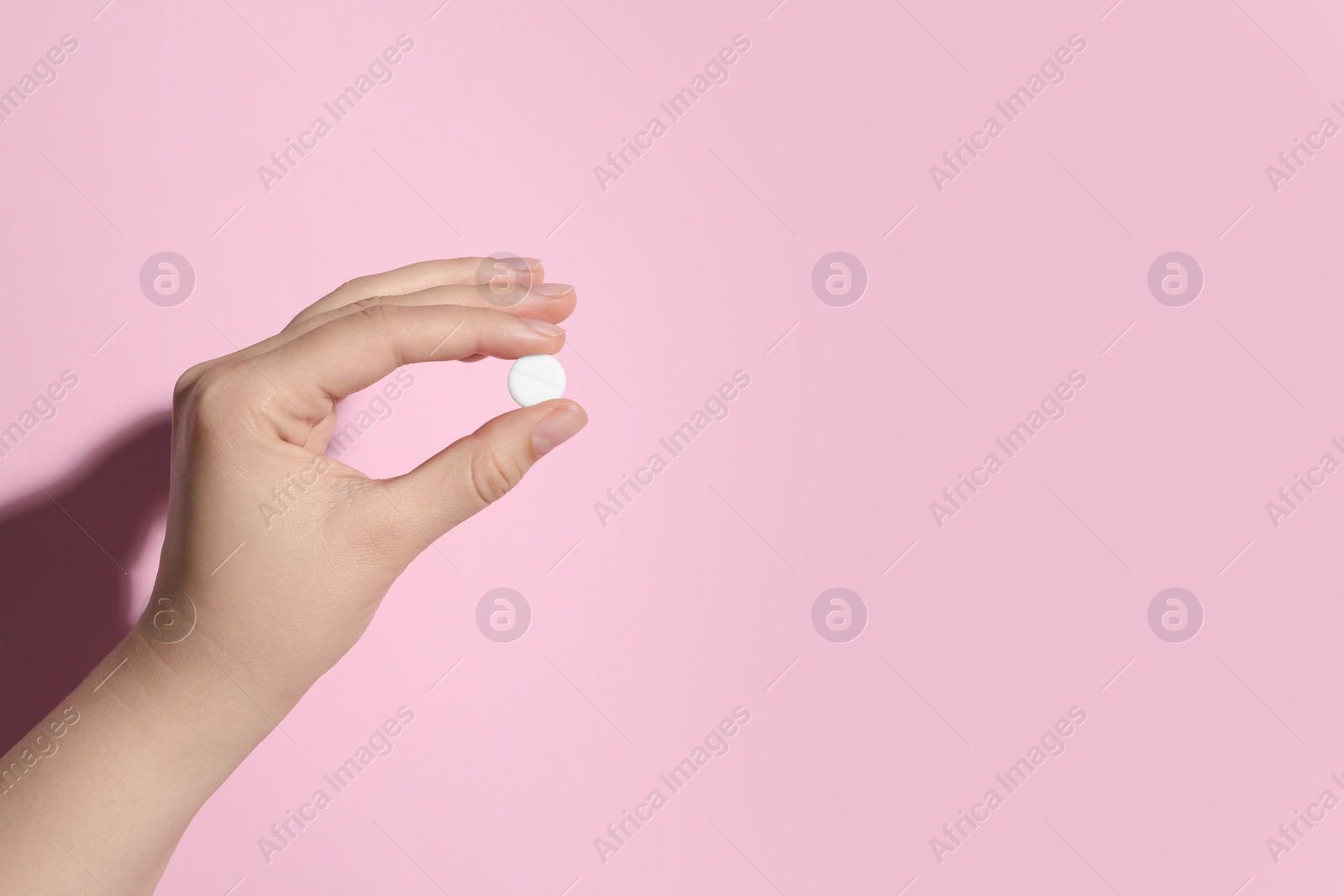 Photo of Woman holding pill on pink background, closeup. Space for text