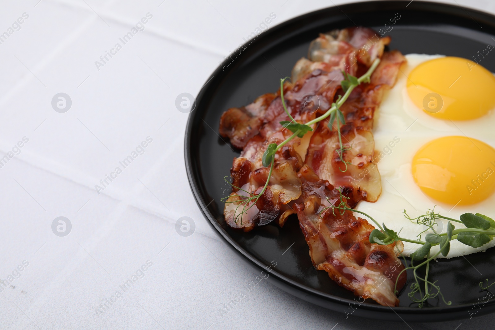 Photo of Fried eggs, bacon and microgreens on white tiled table, space for text