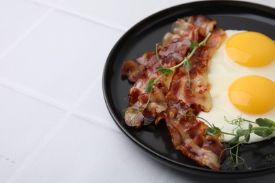 Fried eggs, bacon and microgreens on white tiled table, space for text