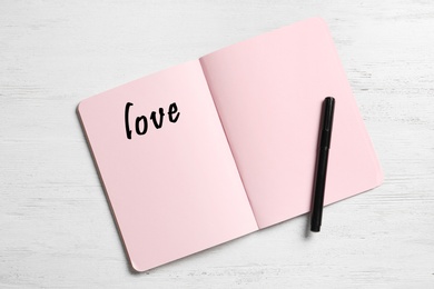 Image of Word Love written in notebook with pink pages on white wooden background, top view