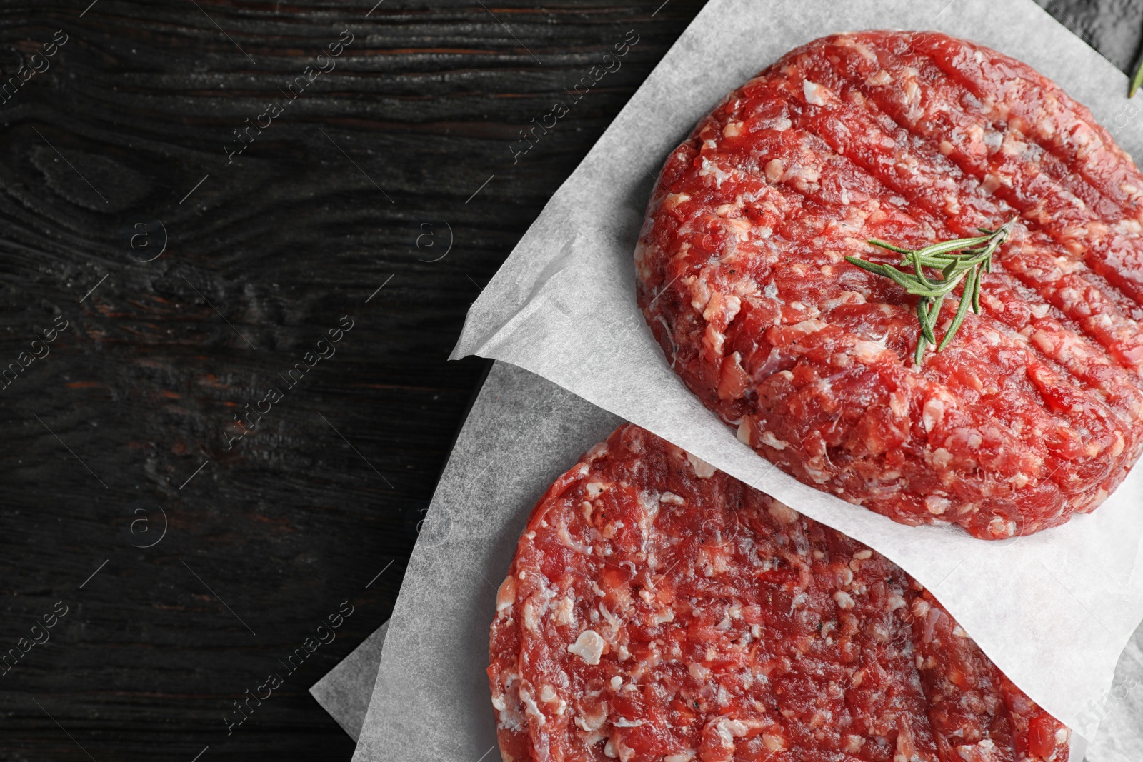 Photo of Raw meat cutlets for burger on black wooden table, top view. Space for text