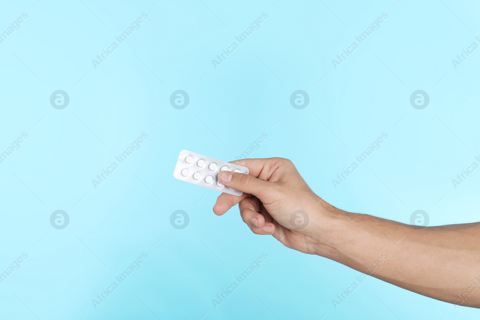 Photo of Young man holding pills on color background, closeup with space for text. Medical object