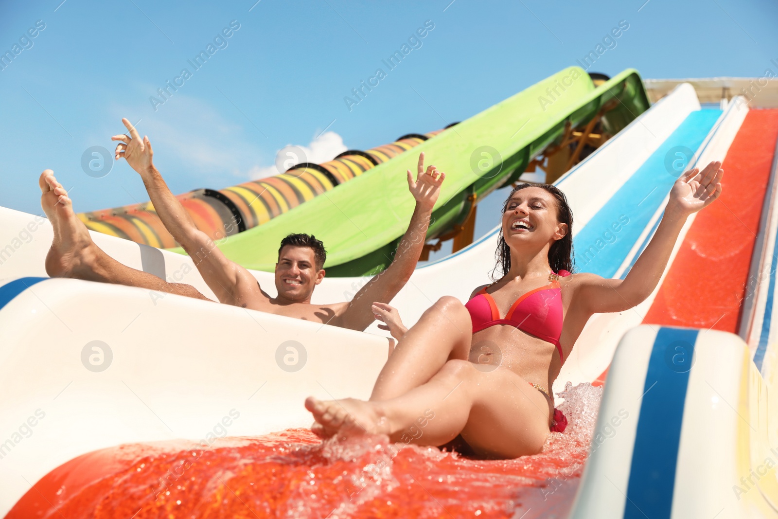 Photo of Happy couple on slide at water park, low angle view. Summer vacation