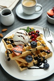Photo of Delicious Belgian waffles with ice cream, berries and chocolate sauce served on grey textured table, closeup