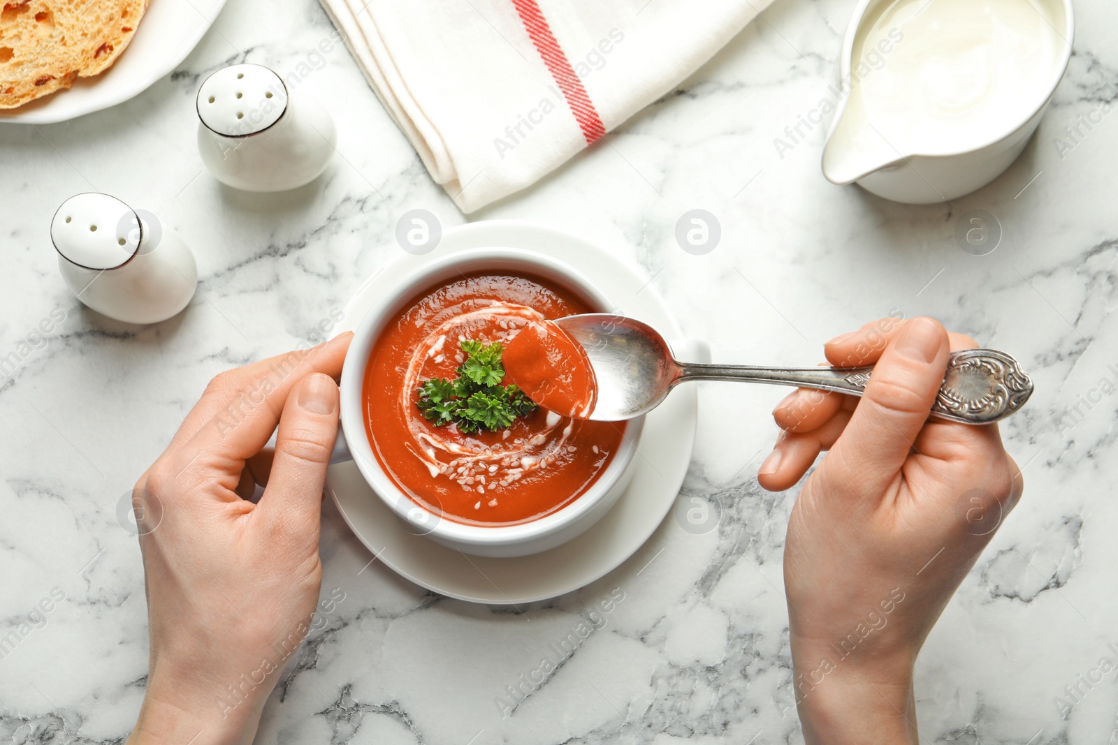 Photo of Woman eating fresh homemade tomato soup at marble table, top view