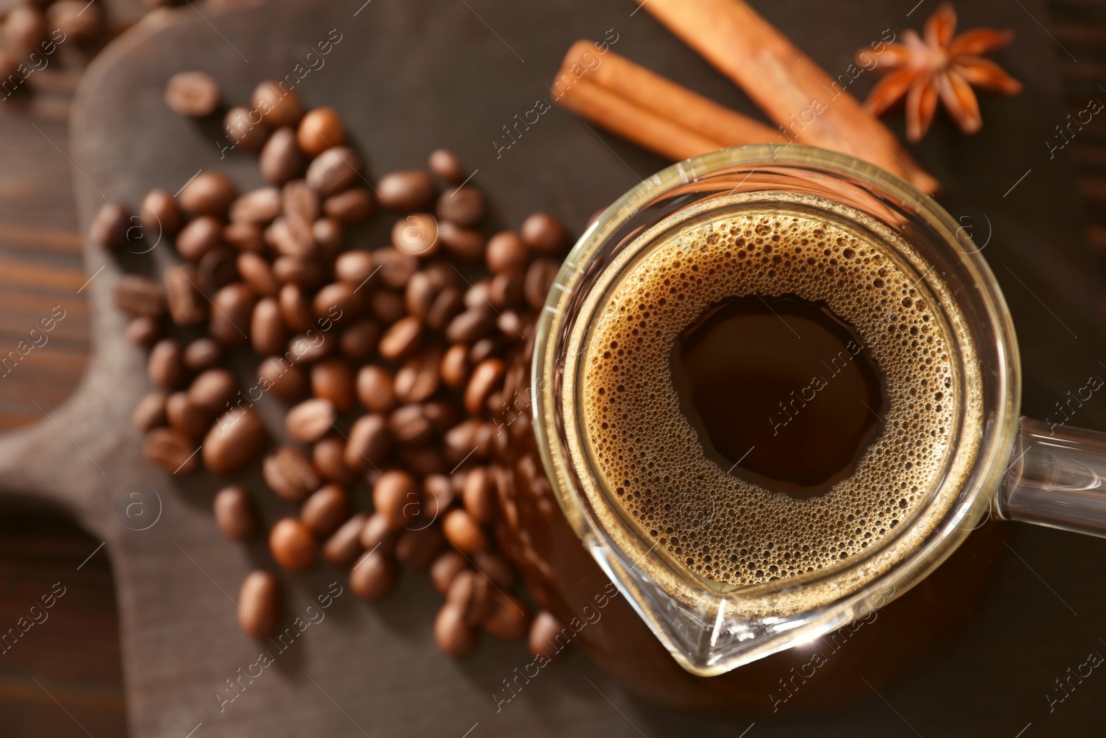 Photo of Glass turkish coffee pot with hot drink and beans on wooden table, top view. Space for text