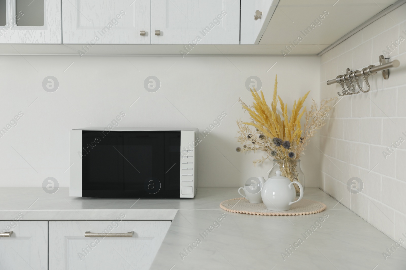 Photo of Modern microwave oven, dry flowers, cup and teapot on countertop in kitchen