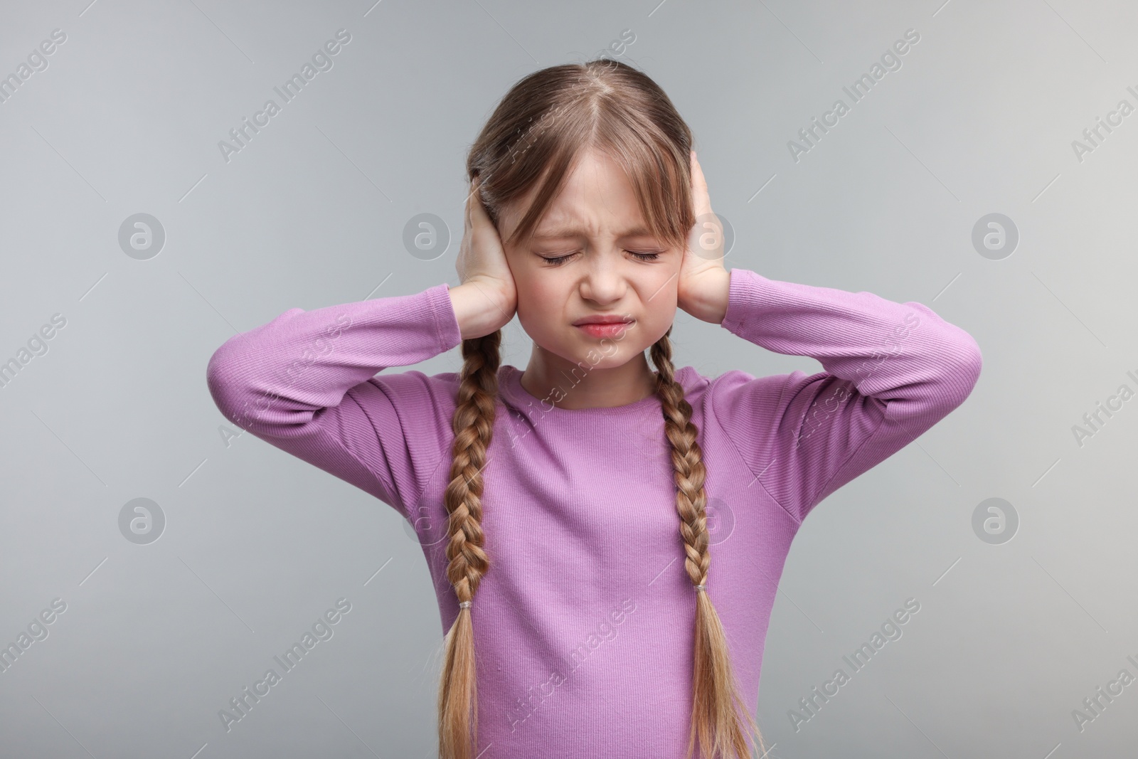 Photo of Hearing problem. Little girl suffering from ear pain on grey background