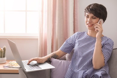 Photo of Young woman talking on mobile phone while working with laptop at home