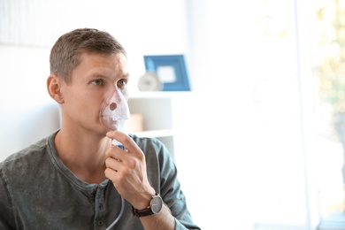 Photo of Young man using asthma machine indoors. Space for text