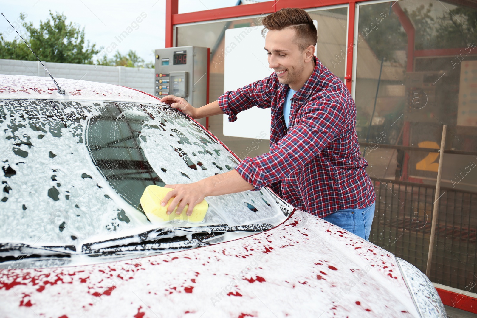 Photo of Young man cleaning vehicle with sponge at self-service car wash