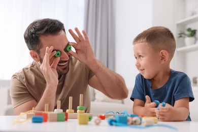 Photo of Motor skills development. Father and his son playing with wooden pieces and string for threading activity at table indoors