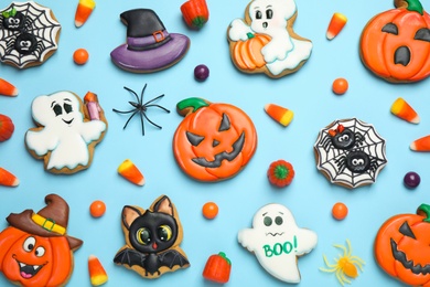 Tasty cookies and sweets for Halloween party on light blue background, flat lay