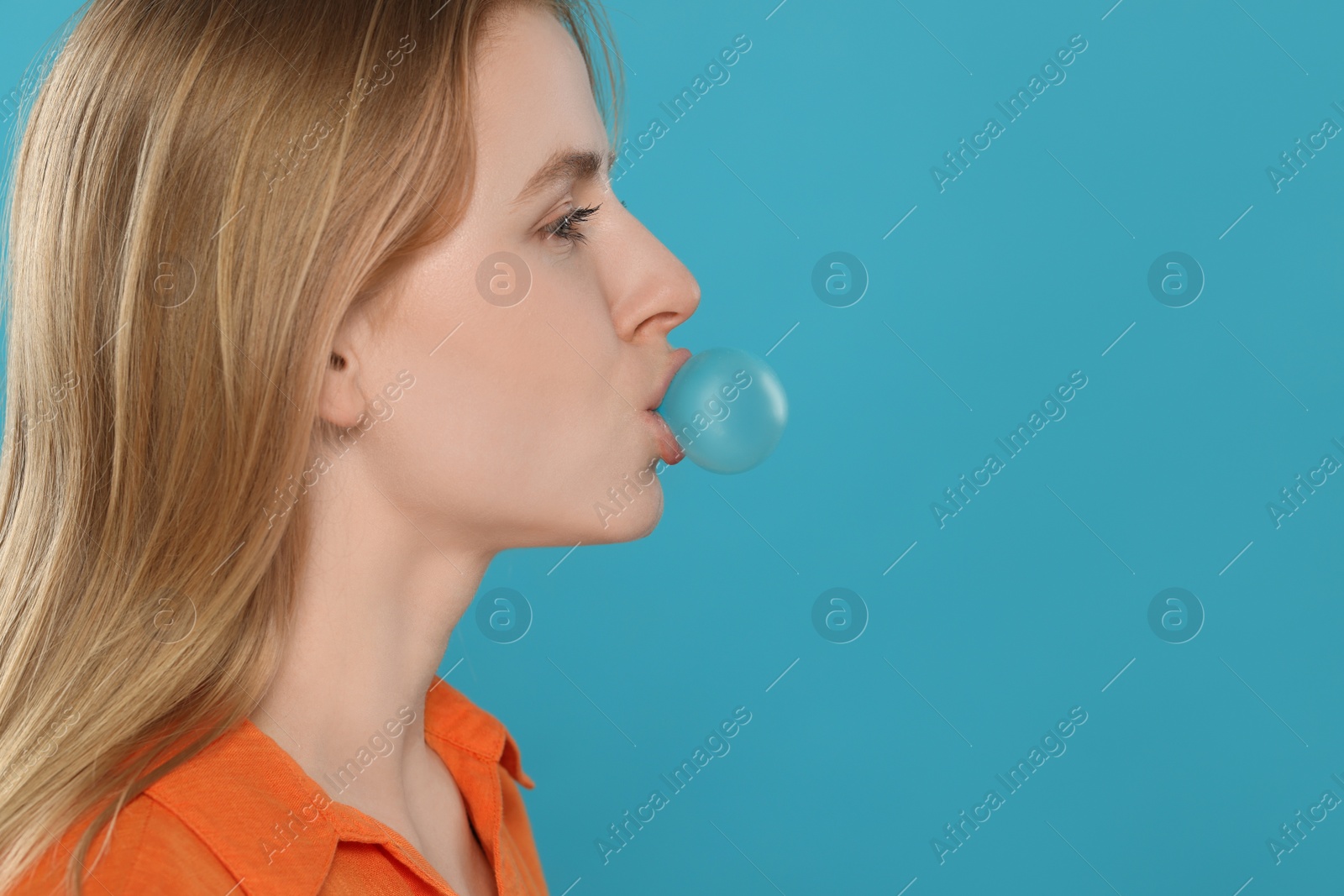 Photo of Beautiful young woman blowing bubble gum on light blue background. Space for text