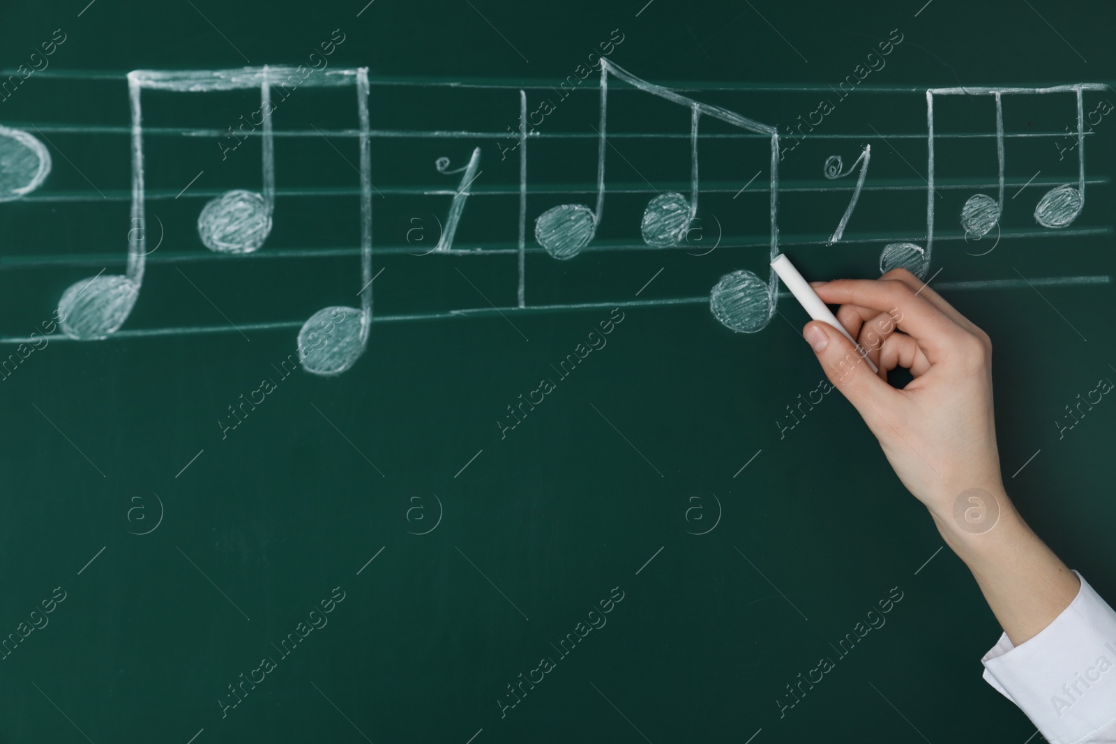 Photo of Woman writing music notes with chalk on blackboard, closeup