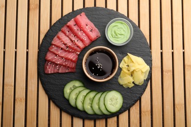 Photo of Tasty sashimi (pieces of fresh raw tuna), sliced cucumber, soy sauce, wasabi and ginger slices on wooden table, top view