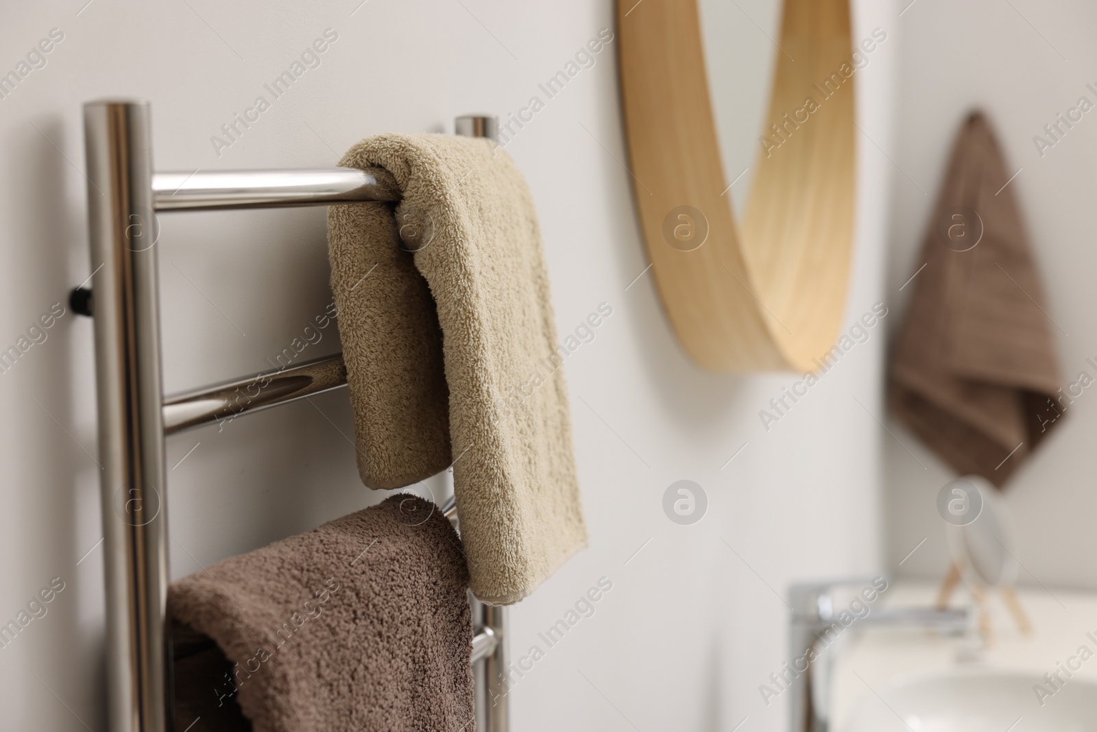Photo of Heated towel rail with brown towels in bathroom, closeup