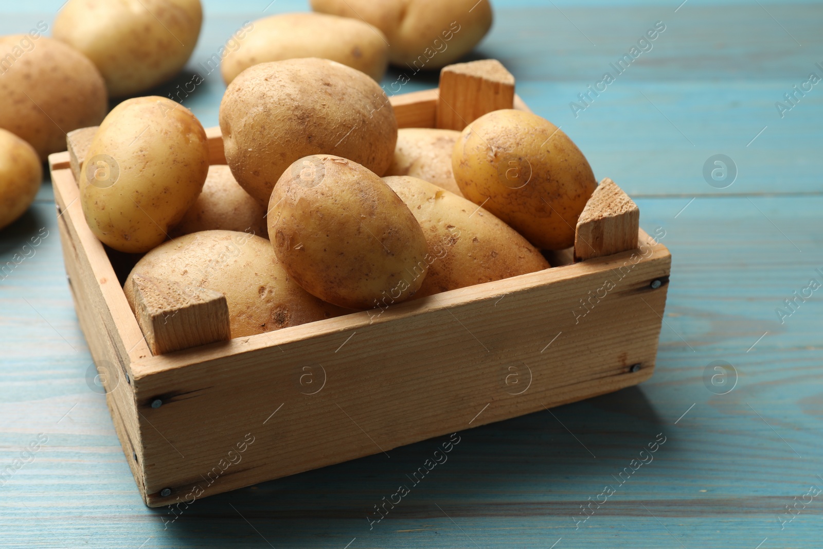 Photo of Raw fresh potatoes in crate on light blue wooden table