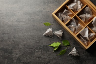 Photo of Wooden box with paper tea bags and leaves on black table, flat lay. Space for text