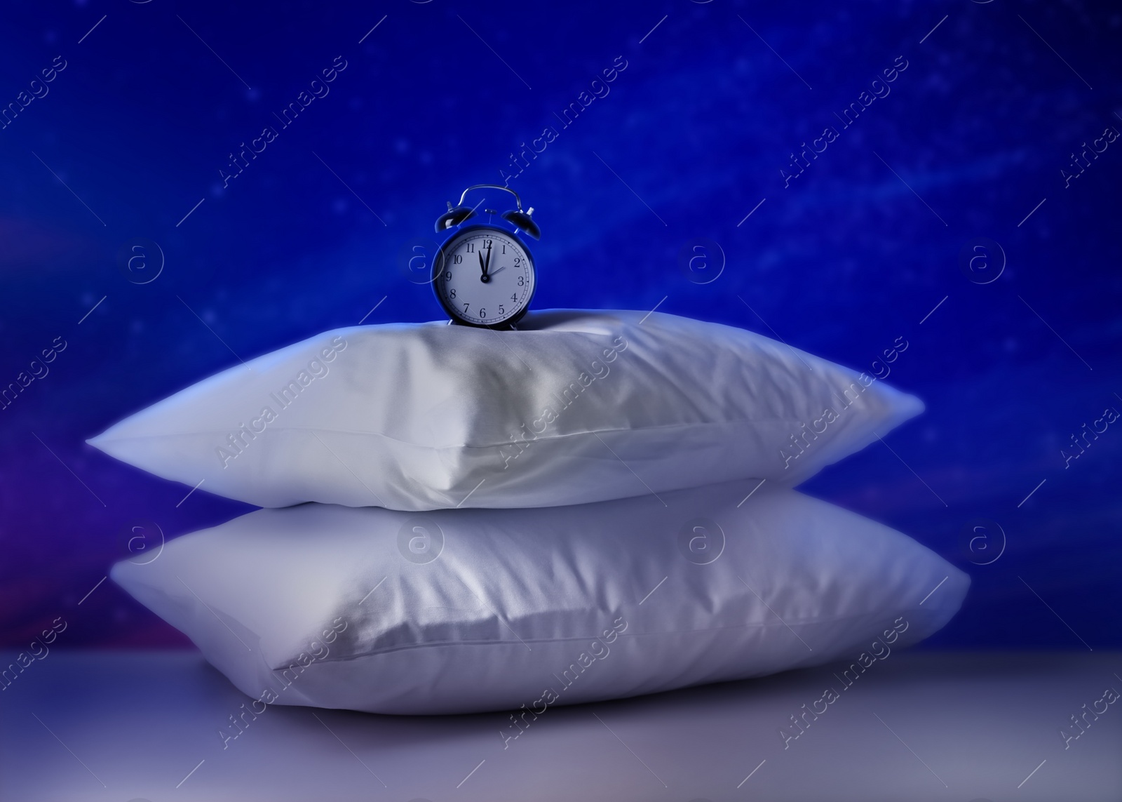 Image of Soft pillows and alarm clock on light grey table against night sky with stars. Insomnia