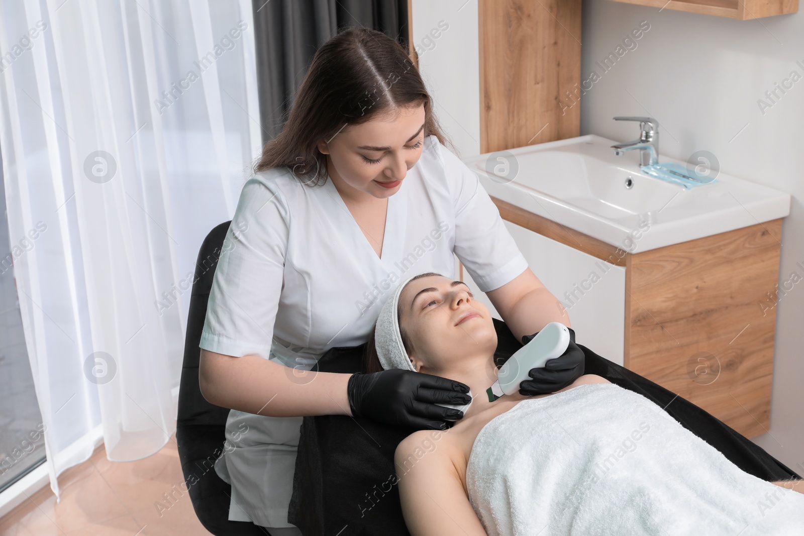 Photo of Cosmetologist using ultrasonic scrubber. Client having cleansing procedure in clinic