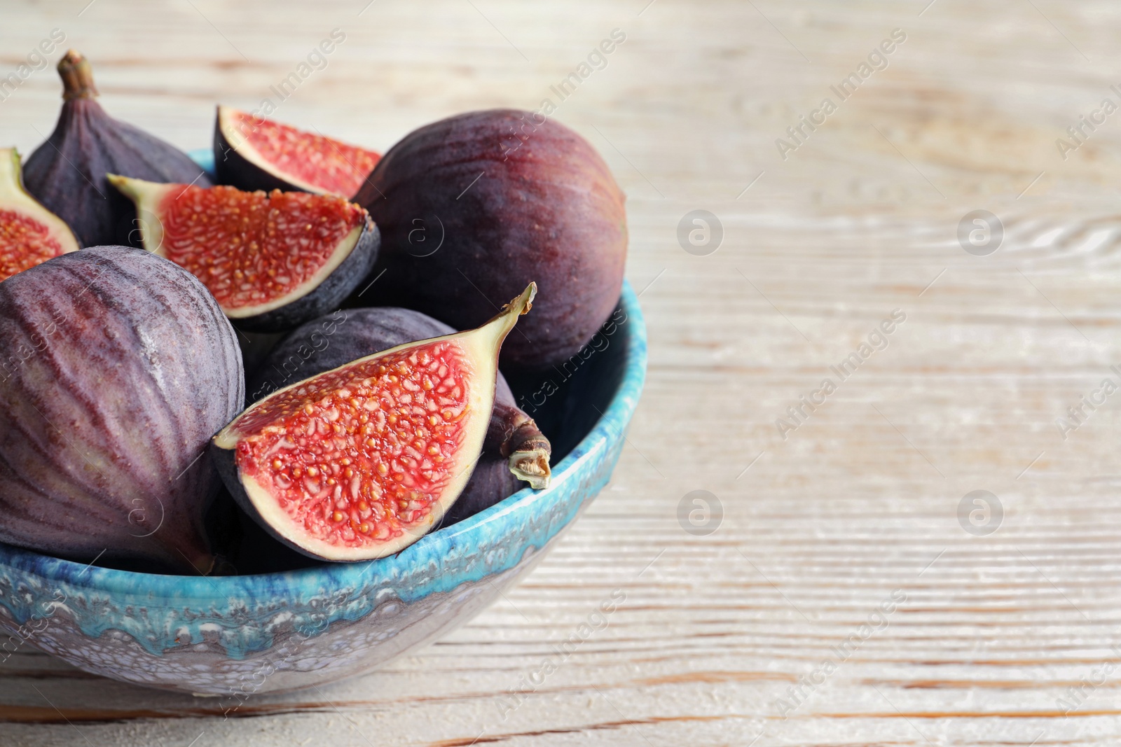 Photo of Bowl with fresh ripe figs on wooden background. Space for text