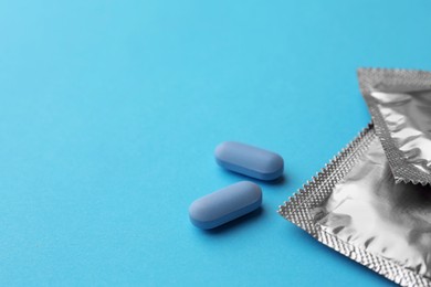 Photo of Pills and condoms on light blue background, space for text. Potency problem