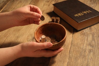 Donate and give concept. Woman putting coin into bowl at wooden table, closeup