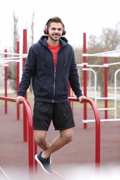 Young man with headphones listening to music and exercising on sports ground