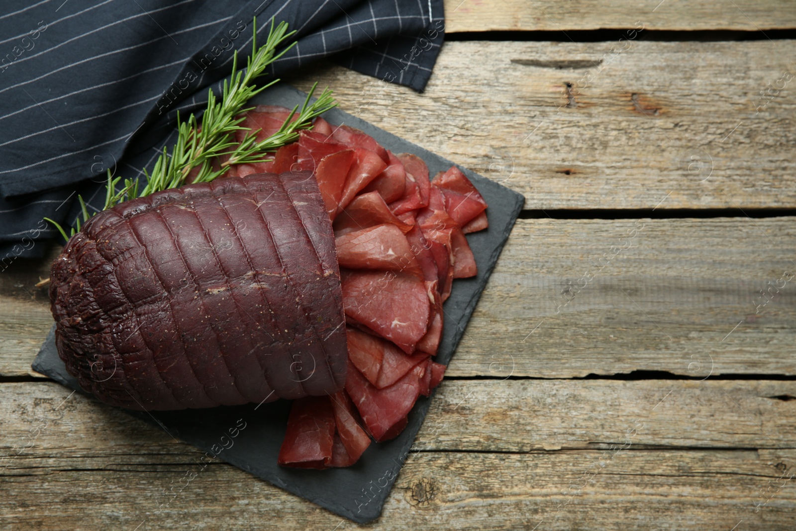 Photo of Tasty bresaola and rosemary on wooden table, top view. Space for text