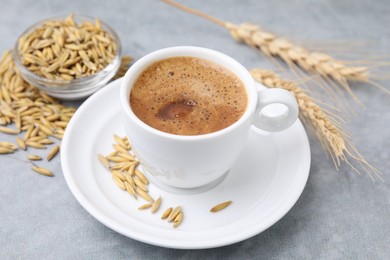 Photo of Cup of barley coffee, grains and spikes on gray table, closeup